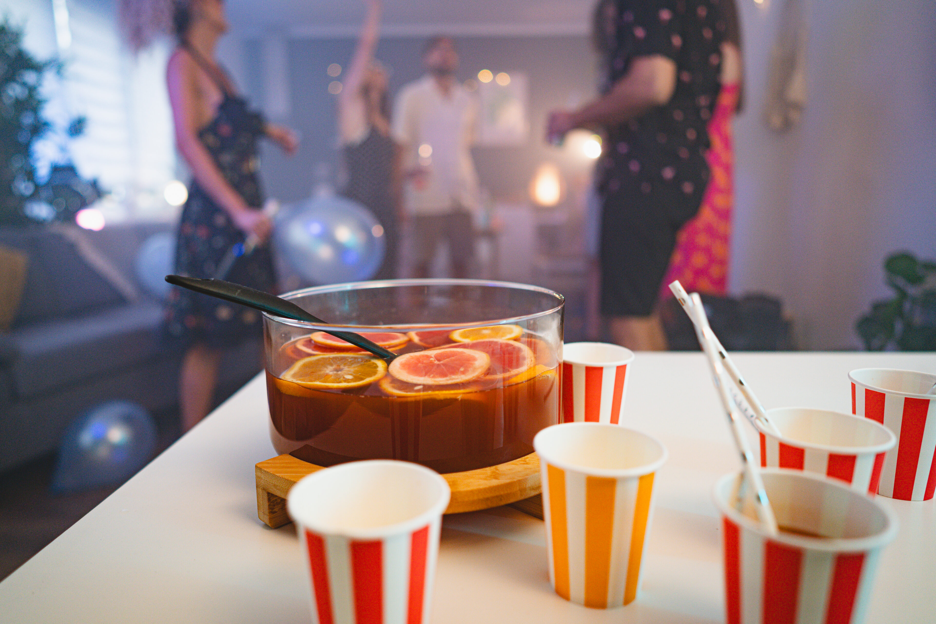 Punch is on the table, while in the background group of Caucasian people dancing during an house party