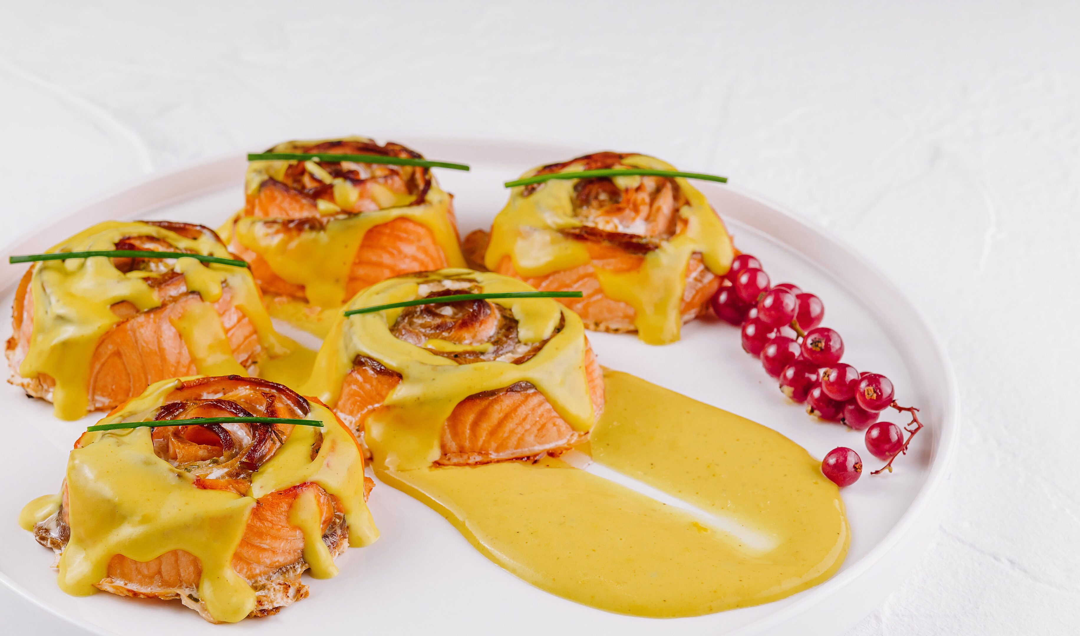 Elegant salmon bites with creamy hollandaise garnished with herbs, on a white plate