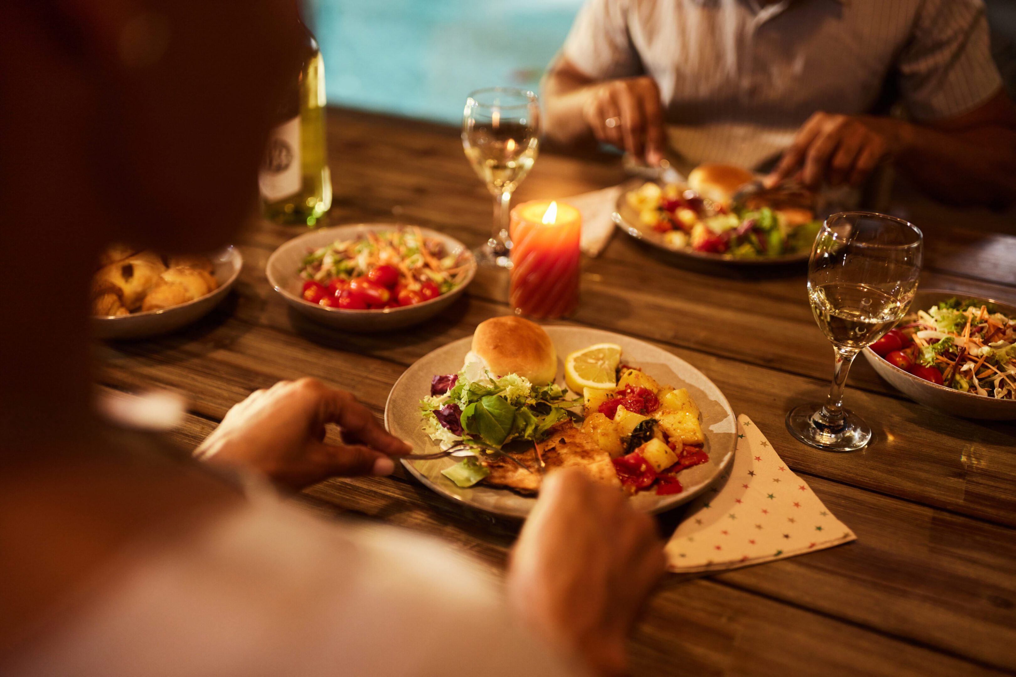 Close up of unrecognizable black woman cutting meat during dinner with her husband at dining table.