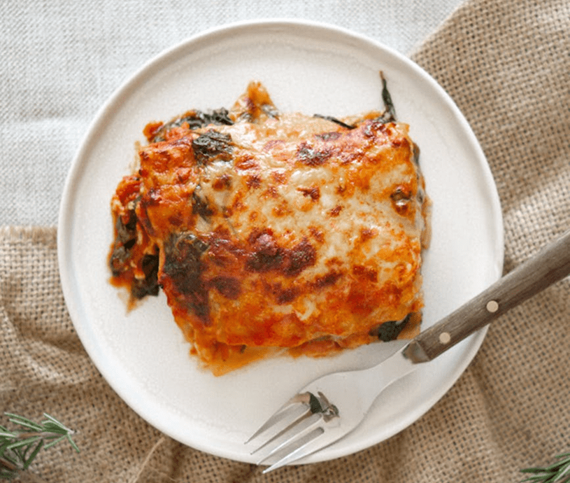 Plate of lasagna with fork on burlap.