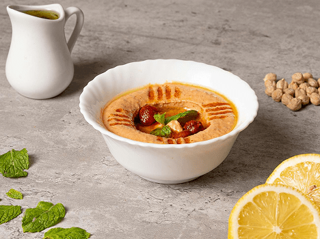 Bowl of hummus with garnishes and lemons.