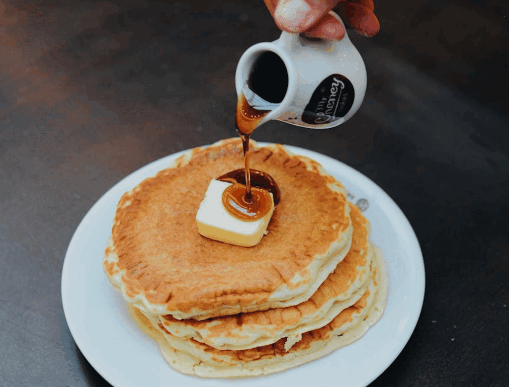 Pouring syrup on pancakes with butter.