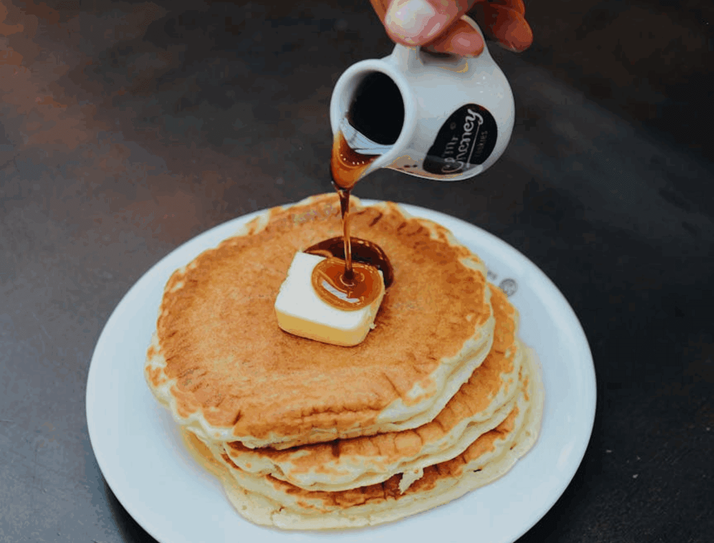 Pouring syrup on pancakes with butter.